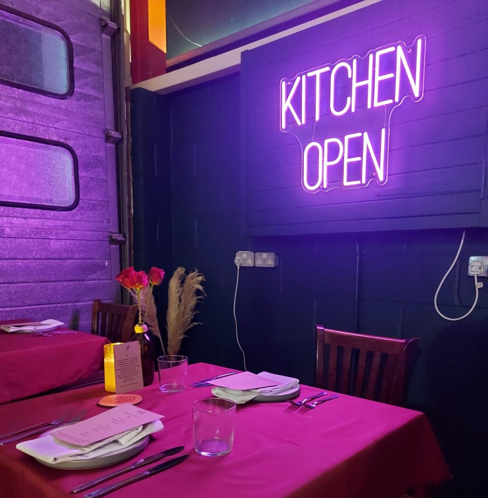 Table set for dinner beneath the pink Kitchen Open neon sign at Eat Street HQ